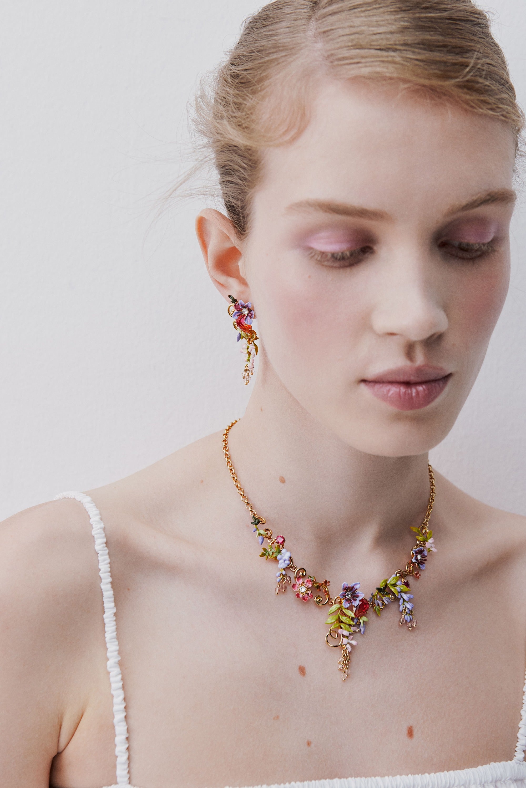 Statement necklace with pink and purple wisteria on a golden arabesque, adorned with ivy and dangling faceted pink crystal beads